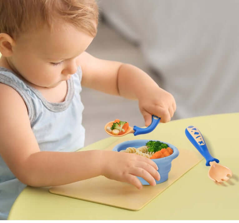 Baby learning to eat using curved fork and spoon set with food in blue bowl