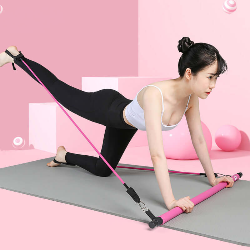 Woman using pink Pilates fitness bar with elastic ropes for exercise on a yoga mat in a pink room.
