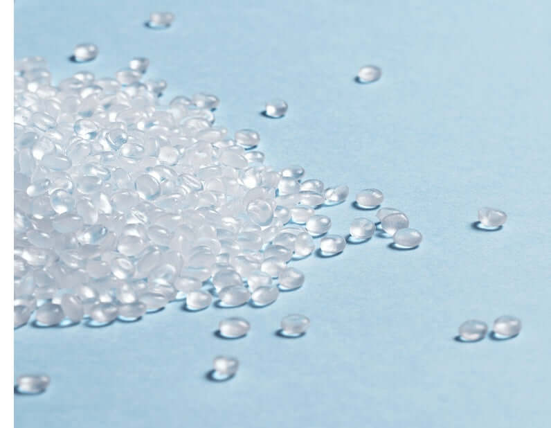 Transparent polypropylene (PP) plastic pellets on a light blue surface for manufacturing baby products.