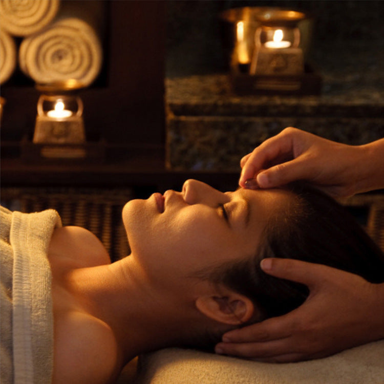 Person receiving a relaxing head massage in a serene spa setting with warm candlelight ambiance.