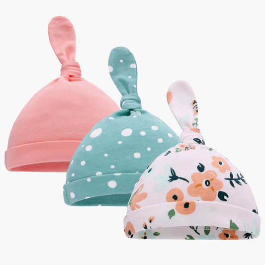 Three baby hats made of pure cotton in pink with flowers, teal with white dots, and white with floral designs, ideal for babies in spring and autumn.