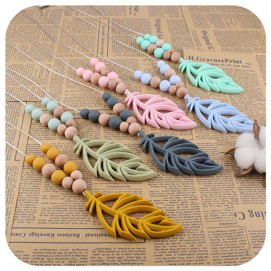 Silicone leaf teether necklaces in assorted colors including mint green, pink, blue, gray, turmeric, on a brown background.