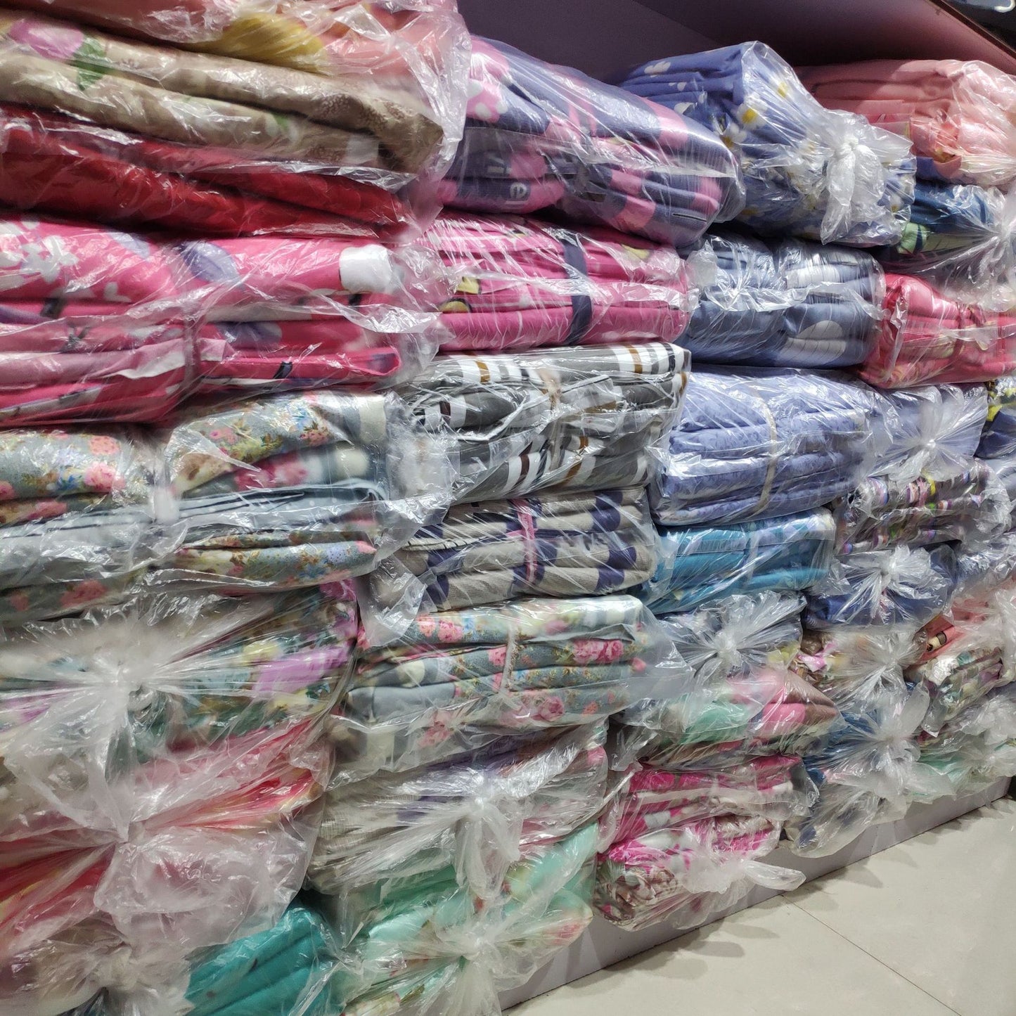 Stacks of colorful packaged bedding sets on display in a store, featuring various patterns and vibrant designs.