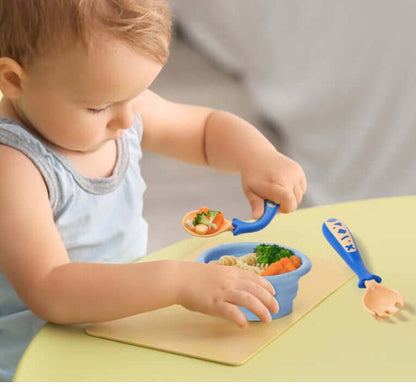 Baby learning to eat using curved fork and spoon set with food in blue bowl