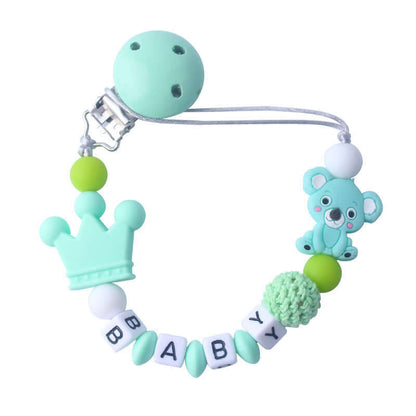 Mint green baby pacifier clip with silicone and wooden beads, featuring a crown and bear design, and "BABY" spelled in white blocks.