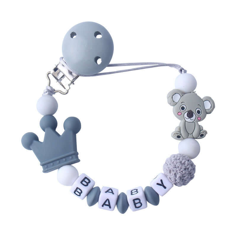 Grey silicone and wood pacifier clip with 'BABY' letters, crown, and koala design. Dummy holder, baby accessory.