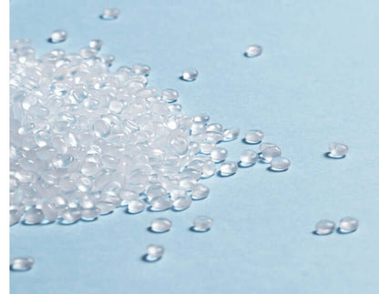 Transparent polypropylene (PP) plastic pellets on a light blue surface for manufacturing baby products.