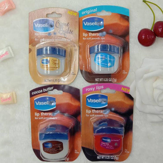 Four types of Vaseline Lip Therapy displayed on a soft surface, featuring original, rosy lips, cocoa butter, and crème brulee variations.
